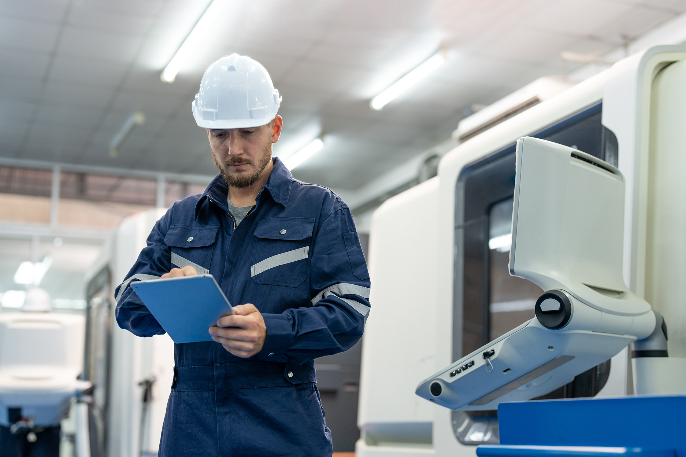 Male engineer using tablet and standing at factory. Man technician wearing uniform and helmet safety operator CNC machine in workshop heavy metal industrial.